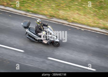 OSTRAVA, TCHÉQUIE - 14 NOVEMBRE 2023 : homme avec casque sur scooter ABS Downtown 125i noir avec effet de flou de mouvement Banque D'Images
