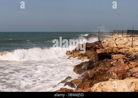 L'océan est rugueux et les rochers sont déchiquetés. Les vagues s'écrasent contre les rochers, créant une scène puissante et dynamique. La scène est une de force Banque D'Images