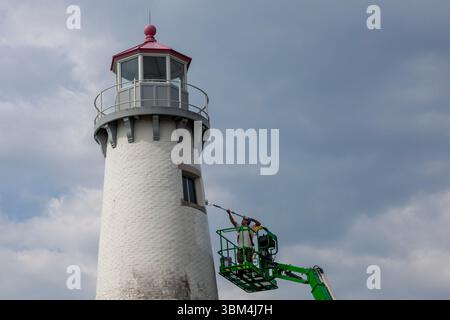 Detroit, Michigan - Un travailleur sur un ascenseur peint le phare du parc d'État de Milliken. Le phare est situé sur la rivière Détroit, près du centre-ville de Détroit. Banque D'Images