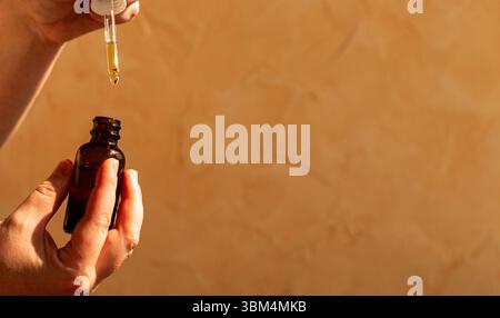 Femme main à l'aide d'une pipette pour distribuer de l'huile faciale de luxe sur fond neutre. Parfait pour les routines de soins de la peau annonces de produits cosmétiques de beauté biologiques. Banque D'Images