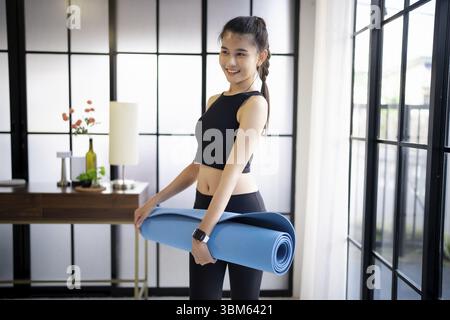 Femme de fitness pliant tapis d'exercice avant de travailler dans le studio de yoga. Tapis de yoga roulant après la formation à un mode de vie sain Banque D'Images