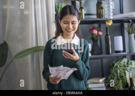Femme asiatique tenant un document papier calculant des économies d'argent payant des factures dans l'application mobile en utilisant le paiement par téléphone intelligent en ligne avec le ménage payant Banque D'Images