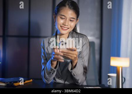 Seul travaillant tard dans la nuit. Femme d'affaires asiatique sur le lieu de travail dans le bureau tard le soir travail à un bureau dans un bureau sombre travaillant sur un ordinateur portable tard dans l'ev Banque D'Images