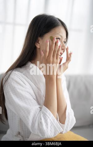 Routine de beauté quotidienne femme asiatique s'auto-soin et se détendre avec silicone sous les patchs oculaires souriant heureux en utilisant le produit de soin de la peau Banque D'Images