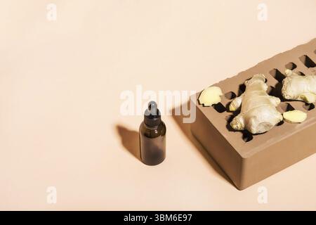 Huile essentielle de gingembre biologique en bouteille en verre foncé, racine de gingembre et brique sur fond beige. Vue isométrique, espace de copie Banque D'Images