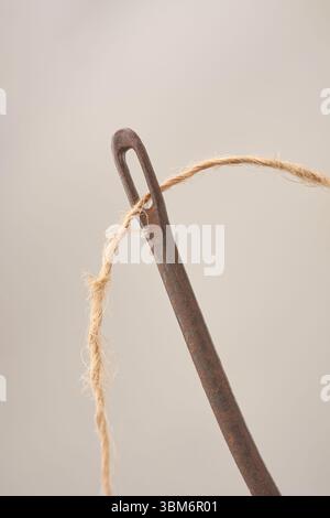 gros plan du fil de coco grossier de noix de coco à travers l'oeil de l'aiguille de sac rouillée ancienne isolé fond gris neutre, concept de matériau naturel et industriel Banque D'Images