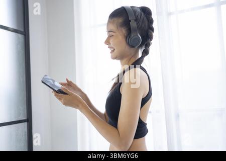 Femme asiatique de fitness utilisant un téléphone intelligent et des écouteurs apprécient écouter de la musique. Femme avec casque smartphone après l'entraînement Banque D'Images