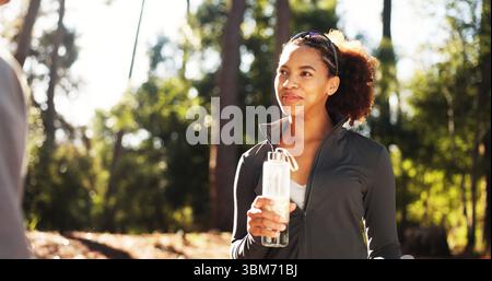 Femme heureuse, forêt et fitness avec bouteille d'eau pour la randonnée, l'hydratation ou la durabilité naturelle. Femme, randonneur africain ou coureur avec le sourire Banque D'Images