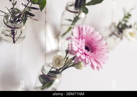 De belles fleurs accrochent sur le mur blanc. DIY Home décor naturel. Les vieux pots en verre sont réutilisés comme vases à fleurs Banque D'Images