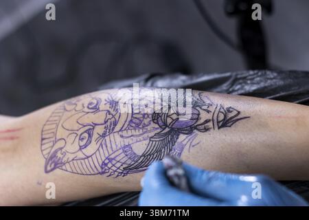 Tatoueur méconnaissable avec tatouage de dessin de machine sur le corps du client méconnaissable dans le salon Banque D'Images