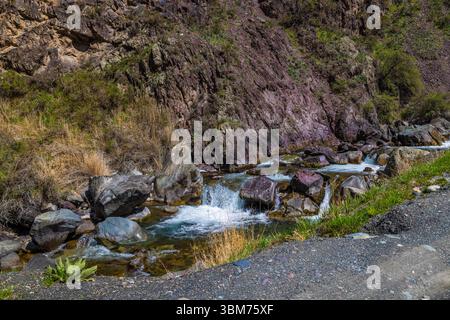 Rivière sereine coulant à travers un paysage montagneux rocheux près de la route de gravier Banque D'Images