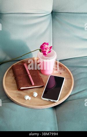 Plan au-dessus du plateau en bois avec ordinateur portable, stylo, téléphone, écouteurs et tasse de boisson rose avec fleur sur canapé. Concept Home Comfort. Banque D'Images