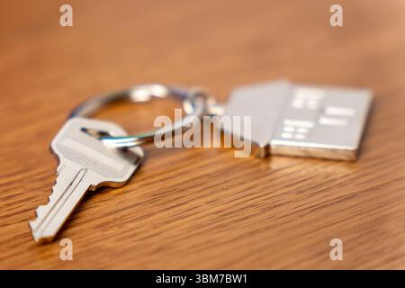 Une clé attachée à un porte-clés métallique en forme de maison sur une table. Propriété, immobilier, propriété et concept de nouveaux départs. Banque D'Images