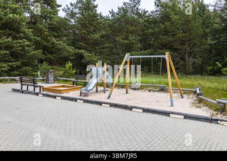 Terrain de jeu de forêt vide avec ensemble de balançoire en bois, toboggan en métal et bac à sable sur la surface pavée du parc Banque D'Images