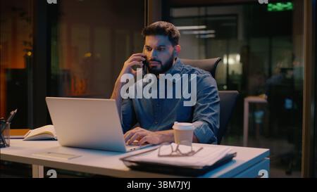 Homme d'affaires indien homme d'affaires multitâche homme d'affaires dans la nuit tard le travail d'heures supplémentaires de bureau parlant appel de téléphone mobile discuter du commerce d'ordinateur portable Banque D'Images