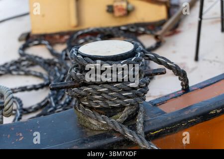 Borne marine enveloppée dans une épaisse corde torsadée sur un pont de bateau, capturant les détails de gréement et la texture robuste. La scène évoque le travail maritime et le quai Banque D'Images