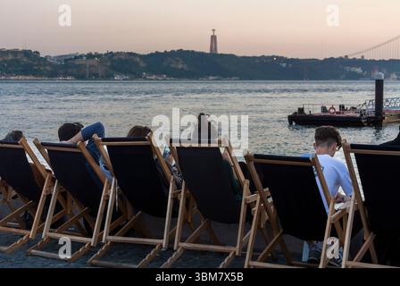 Lisbonne, Portugal, Groupe de touristes, de derrière, assis dans des chaises longues sur la plage, rivière Lisbonne vue générale Banque D'Images