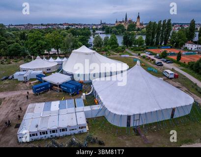 Schwerin, Allemagne. 24 juin 2025. Les acteurs, musiciens et techniciens du Théâtre d'État de Mecklembourg travaillent dans trois tentes et conteneurs spéciaux et répètent pour l'opérette 'la veuve joyeuse'. (Vue aérienne avec un drone). En raison de travaux de construction importants dans le bâtiment historique de la scène, six productions sont prévues pour la saison 2025/2026 dans la tente de théâtre sur le lac Schwerin. En plus des pièces de théâtre, ballets, opéras et opérettes, l'Orchestre d'État de Mecklembourg jouera également ses concerts dans la tente. Crédit : Jens Büttner/dpa/Alamy Live News Banque D'Images