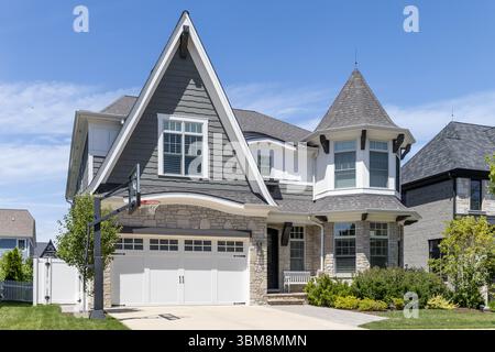 Une maison de style victorien moderne grise et blanche avec un toit incliné, une tourelle et un parement rocheux au premier étage. Banque D'Images