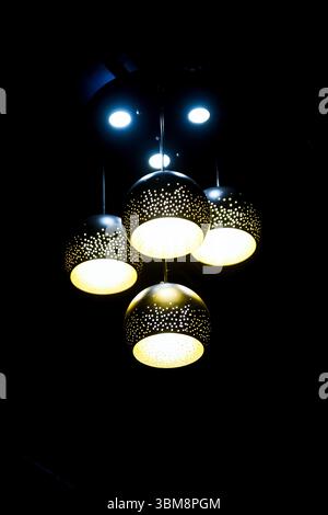 Quatre élégantes suspensions suspendues au plafond projettent une lumière chaleureuse dans un cadre contemporain. Banque D'Images