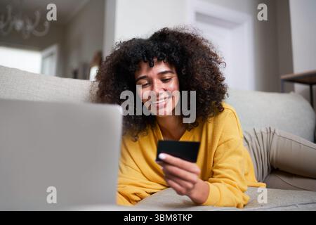 Femme souriante shopping en ligne avec carte de crédit sur canapé confortable Banque D'Images