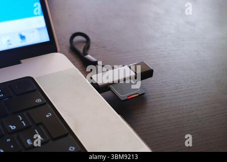 Carte SD lecteur de stockage connecté à un ordinateur portable avec un connecteur de lecteur de carte USB sur un bureau en bois. Banque D'Images