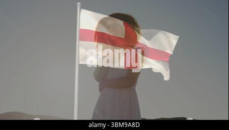 Face à une femme portant une robe blanche sans manches sur une colline aride à l'aube, avec le drapeau de la croix de St George. Silhouette, patriotisme, sérénité, paysage, mini Banque D'Images