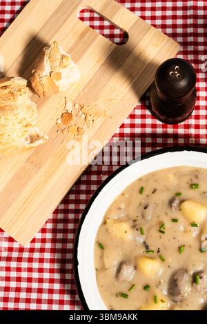 Soupe crémeuse de pommes de terre aux champignons et à la ciboulette servie sur une nappe à carreaux avec du pain Banque D'Images