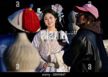 Femme en robe traditionnelle chinoise souriant derrière ventilateur de dentelle pendant la séance photo Banque D'Images