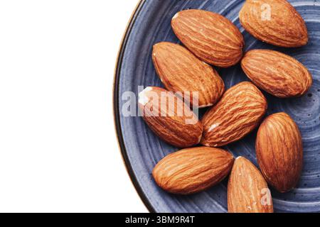 Amandes sur plaque bleue. Collation saine et nourriture naturelle. Gros plan de noix brunes entières. Source de protéines végétaliennes. Ingrédient organique pour l'alimentation et la cuisine. Banque D'Images