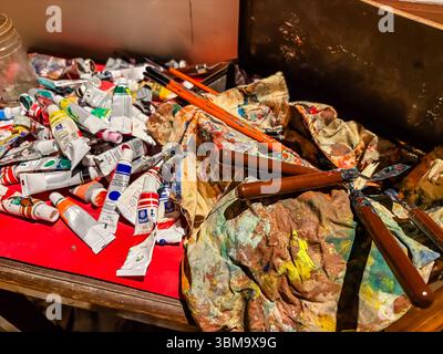 Fournitures artistiques. Gros plan de tubes de peinture, pinceaux et couteaux à palette sur une surface encombrée dans un studio d'artiste, montrant le processus créatif. Banque D'Images