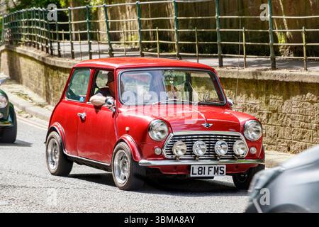 Vintage Red Mini Cooper conduisant dans une rue de la ville avec un mur de pierre et une rampe le long du trottoir. Banque D'Images