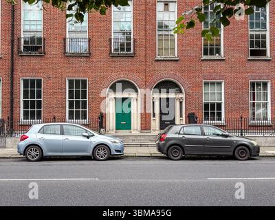 Voitures garées dans la rue, Dublin. Deux voitures garées dans une rue de la ville devant des bâtiments classiques de style géorgien en briques. Banque D'Images