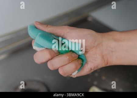 Main de femme au foyer pressant l'eau savonneuse de l'éponge pendant le nettoyage du poêle à gaz sale, pour enlever la saleté et la graisse, favorisant l'hygiène et la propreté dans Banque D'Images