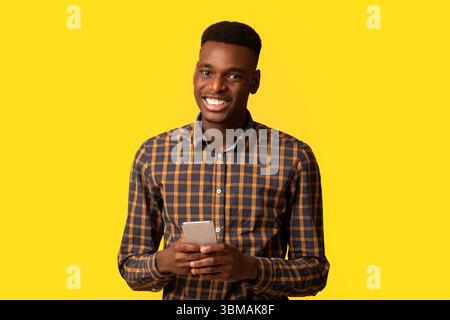 Portrait d'un homme noir heureux avec un smartphone dans les mains souriant à l'appareil photo Banque D'Images