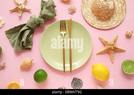 Belle table avec assiette, couverts dorés, serviette et agrumes sur fond rose Banque D'Images