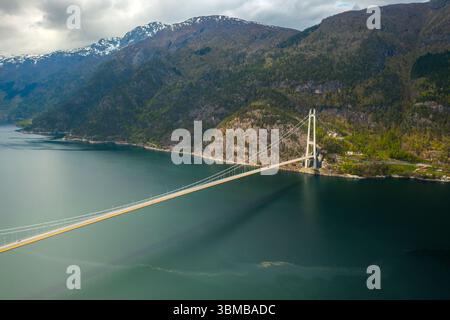 Hardanger Bridge enjambe gracieusement un vaste corps de fjord avec des montagnes imposantes formant une toile de fond spectaculaire. Pont suspendu moderne avec des tours proéminentes Banque D'Images