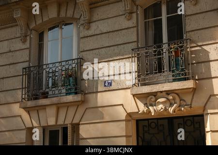 Gros plan détaillé de la façade d'un immeuble parisien, présentant deux balcons avec des balustrades en fer ornées, des plantes en pot et une élégante victoire Banque D'Images