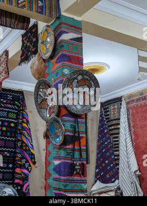 Maroc, Merzouga, 04 juillet 2025. Intérieur d'un magasin de tapis berbère dans le sud du Maroc, avec des textiles colorés et des plateaux décoratifs en métal accrochés à un Banque D'Images