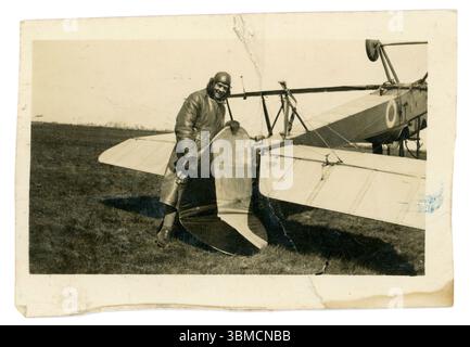 Avion original de l'ère WW1 avec un pilote joyeux possiblement du Royal Flying corps (RFC) en équipement volant, y compris un long trench-coat en cuir, une casquette en cuir et des gants, debout à côté de son avion à l'envers, qui s'est retourné et s'est écrasé - il tient la queue cassée et sourit. 1914-1918 Banque D'Images
