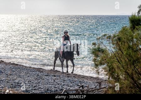 Rhodes, Grèce. Une touriste monte à cheval le long d'une plage. le cheval marche près du rivage. Une randonnée équestre organisée Banque D'Images