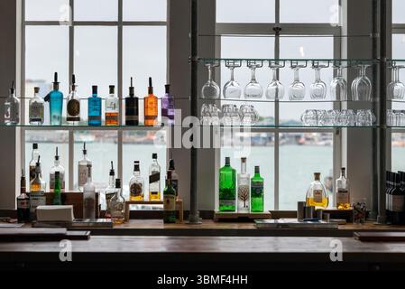 Des bouteilles de boisson et divers verres sur une étagère de bar donnant sur un port. Banque D'Images