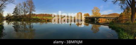 Vue panoramique d'une scène de rivière sereine pendant l'automne avec un pont et des reflets. Banque D'Images