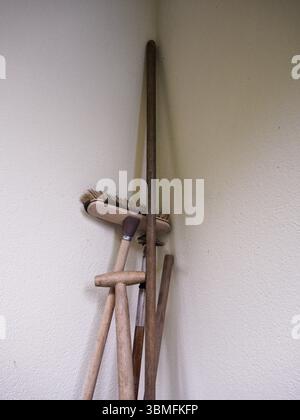Gros plan d'un tas d'outils en bois rustiques placés dans le coin d'une façade de bâtiment, avec des poignées en bois visibles et le dessus d'un balai. Banque D'Images