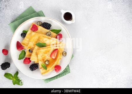 Crêpes fines avec des baies, des feuilles de menthe et du sirop d'érable sur un fond gris. Vue de dessus. Copier l'espace. Banque D'Images
