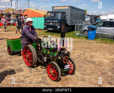 Un homme conduit un moteur de traction à vapeur miniature vintage orné de drapeaux britanniques dans un cadre de festival vintage en plein air Banque D'Images
