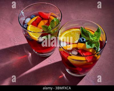 deux verres de sangria rouge avec des morceaux de fruits sur fond rouge foncé Banque D'Images