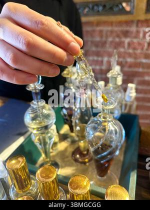 Gros plan de petites bouteilles de parfum artisanal et d'huile essentielle, avec la main d'une femme à l'aide d'une pipette. Banque D'Images