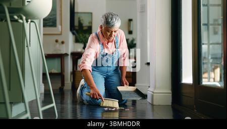 Femme mature, balayant et nettoyant le sol à la maison pour l'enlèvement de la saleté, l'entretien ménager et l'entretien. Travaux ménagers, nettoyant et pelle à poussière dans la maison pour ramasser Banque D'Images