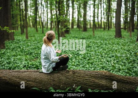 Femme faisant de l'exercice de relaxation et assise dans la position yoga lotus dans la nature. Baignade en forêt et méditation Banque D'Images